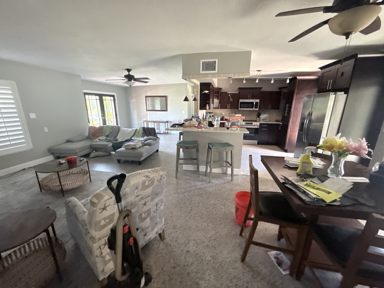 Living and dining area before cleaning, with items across the furniture, table, and kitchen counters